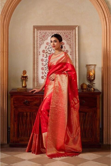Woman wearing red silk saree with golden border in traditional indoor setting